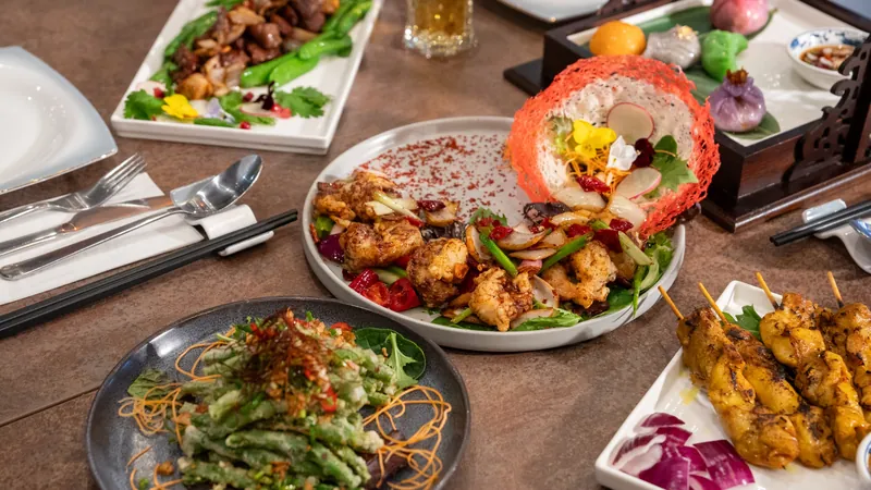 Overhead view of a sharing table with chilli prawns, tempura beans, satay and dim sum